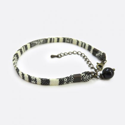 Bracciale in stile etnico fatto a mano, caratterizzato da un ciondolo con una perla di ossidiana, in cordoncino piatto di cotone nero con disegni geometrici bianchi.