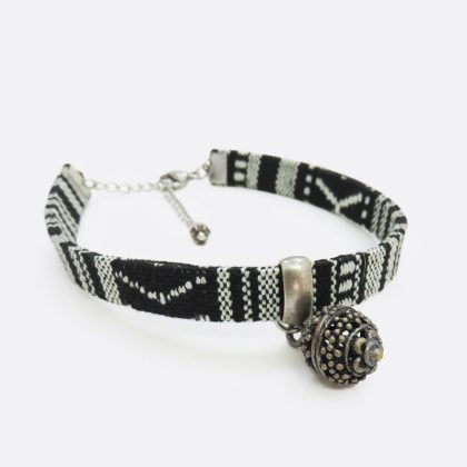 Bracciale in stile etnico con ciondolo, fatto a mano in cordoncino piatto, nero con disegni geometrici bianchi.