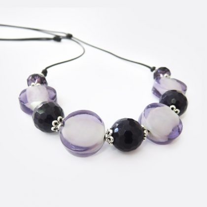Collana realizzata a mano stile boho in cordoncino cerato nero, con perle piatte dalle sfumature viola distanziate da cristalli e perle sfaccettate.