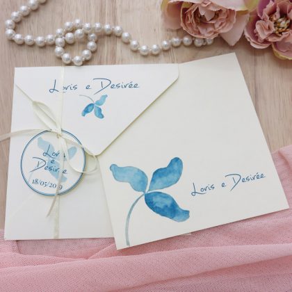 Partecipazione per matrimonio quadrata con illustrazione floreale azzurra con busta personalizzata e nastrino in raso e tag “save the date”.